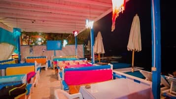 An outdoor seating area with tables and chairs, umbrellas, and a view of the sea.