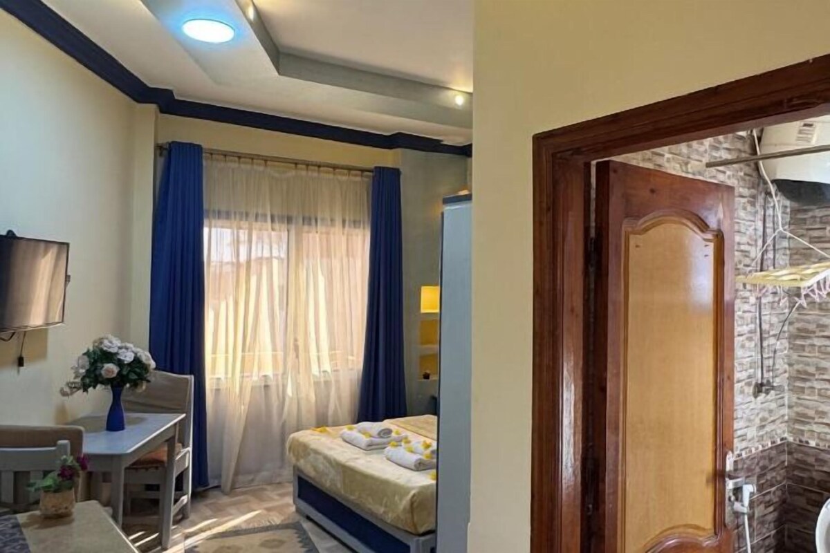 A bedroom with a bed, a desk with a chair, a TV, and a window with curtains.