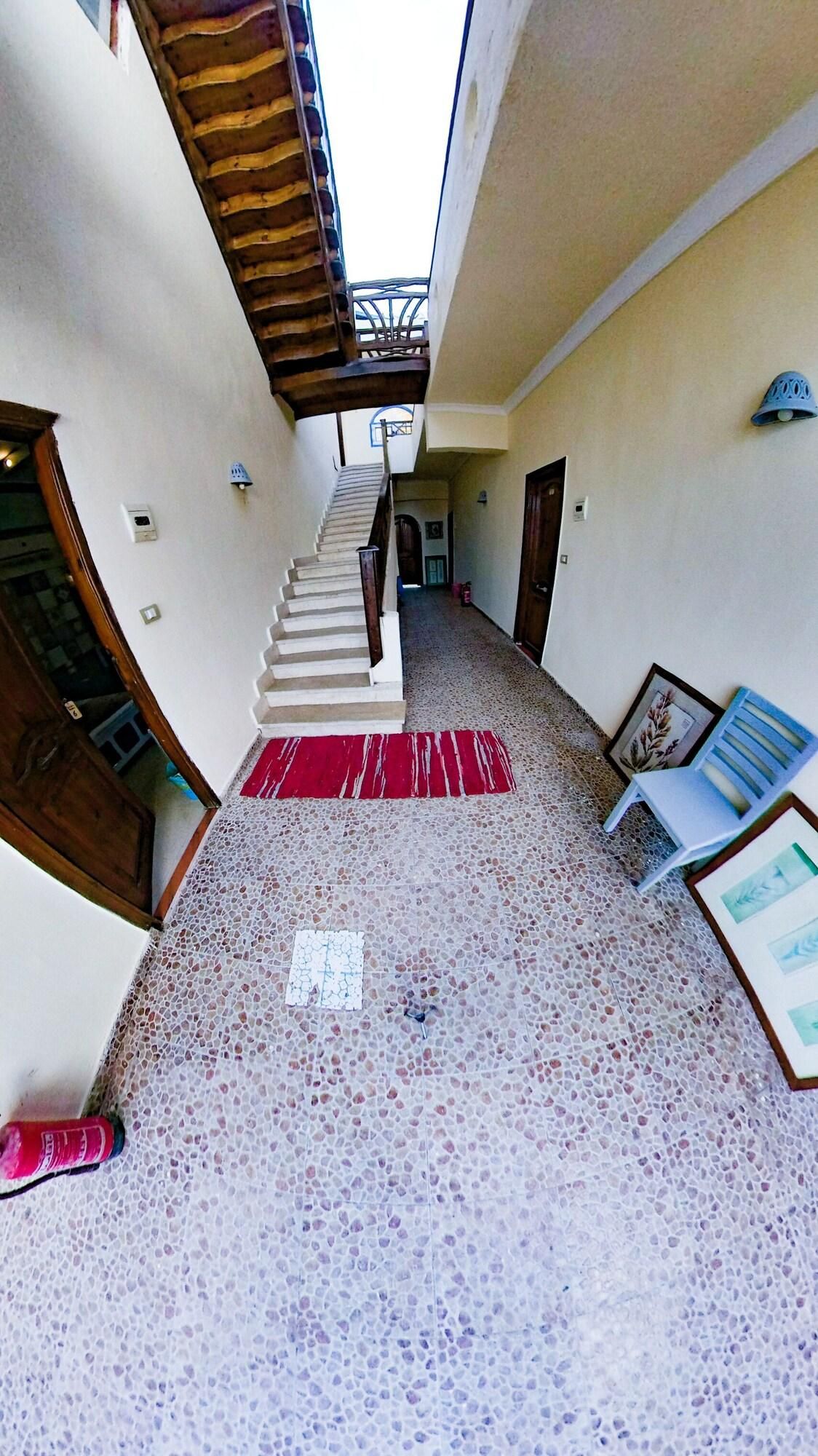 A narrow hallway with a staircase leading to an upper level, a red mat at the bottom, and a framed picture on the right.