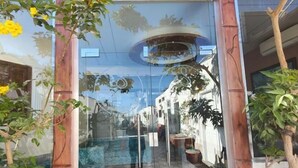 Un ingresso vetrato con pavimento a scacchi, un pilastro in legno e il riflesso di un edificio e del cielo.