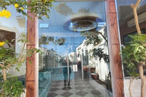 A glass-enclosed entrance with a checkered floor, a wooden pillar, and a reflection of a building and sky. - Sababa Hotel (Dahab)