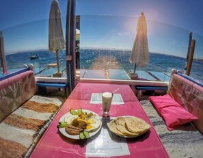 Una mesa con comida y bebida, con vista a una playa con sombrillas y al mar.