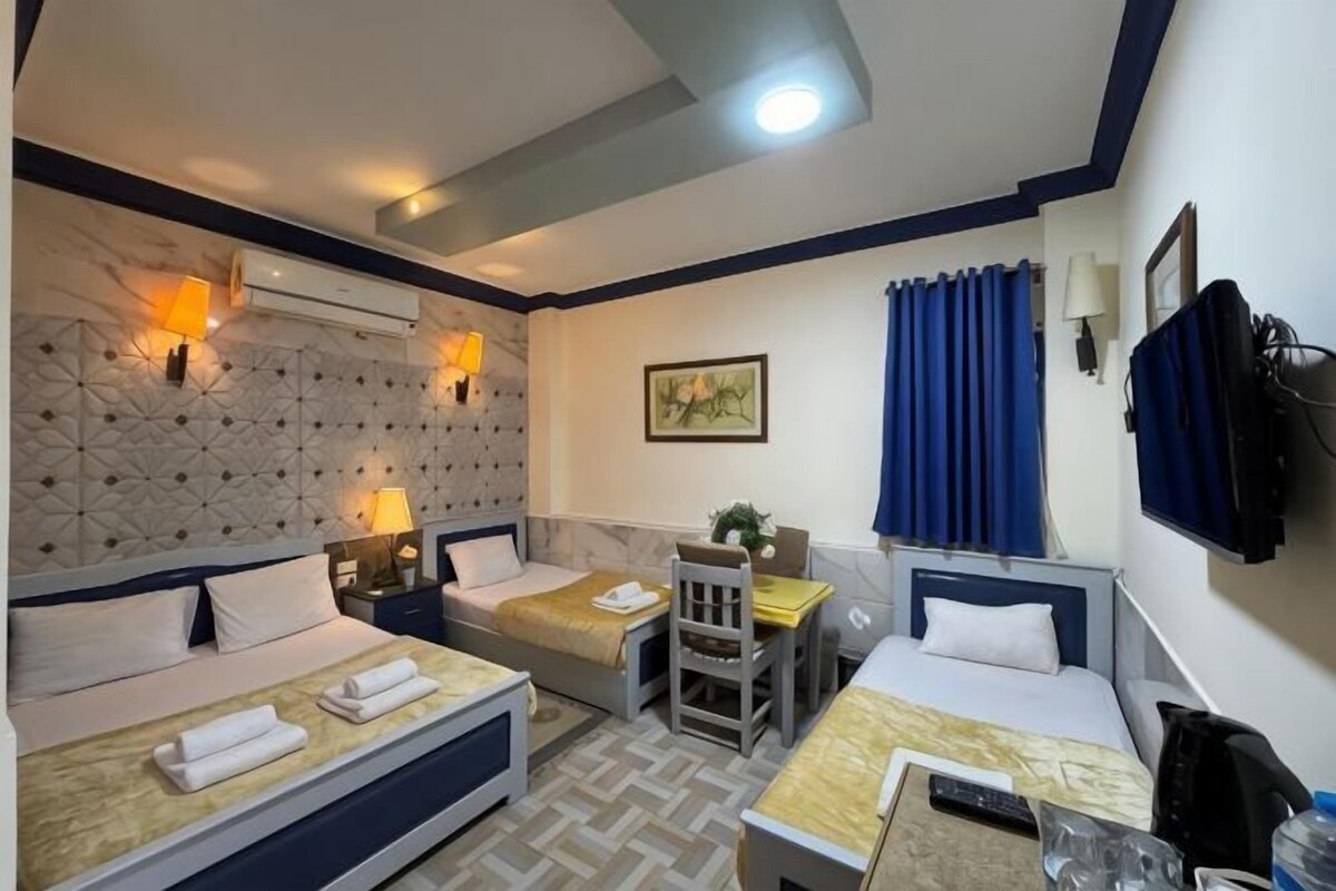 A hotel room with two beds, a desk, a chair, a TV, and a wall-mounted safe.