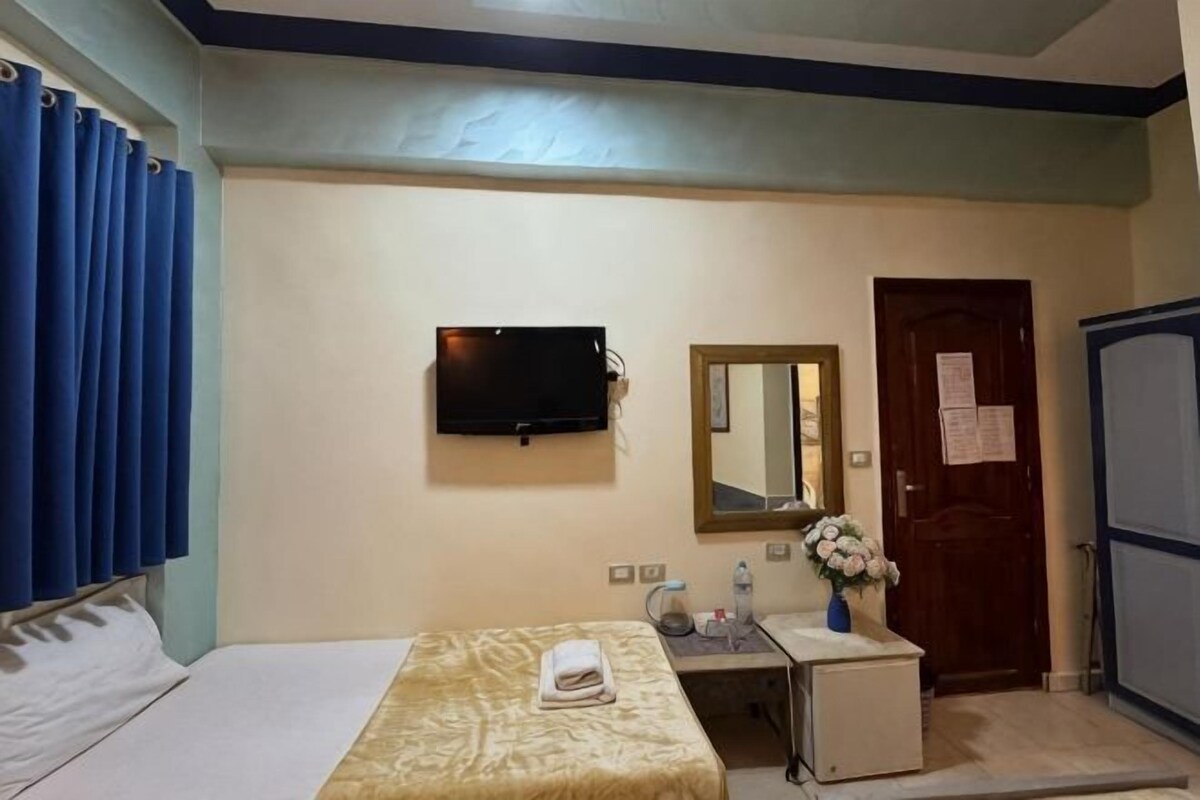 A hotel room with a bed, a desk, a mirror, a television, and a door.