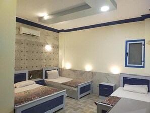 Habitación de hotel con cuatro camas individuales, pared con diseño de mármol, unidad de aire acondicionado y ventana pequeña con marco azul.