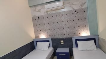 Habitación doble con dos camas, una mesita de noche pequeña, aire acondicionado de pared y una alfombra decorativa.