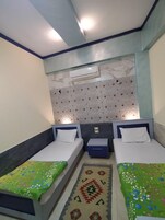 Habitación doble con dos camas, una mesita de noche pequeña, aire acondicionado de pared y una alfombra decorativa.