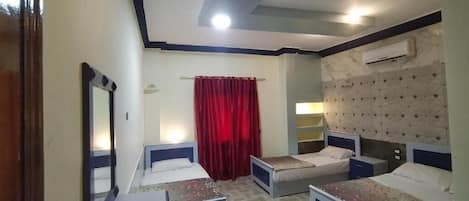 Una habitación de hotel con dos camas individuales, una cortina roja, un equipo de aire acondicionado y un cabecero estampado.