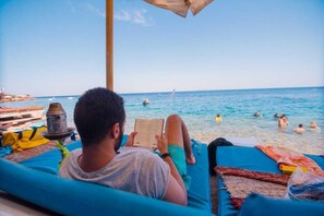 Una persona relajándose en una tumbona de playa con un libro, un narguilé y una toalla.