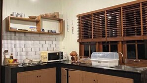 A kitchen with wooden cabinets, a microwave, a sink, and a window with blinds. - "Peace in Ranong: Your Cozy Retreat" (Kapoe)