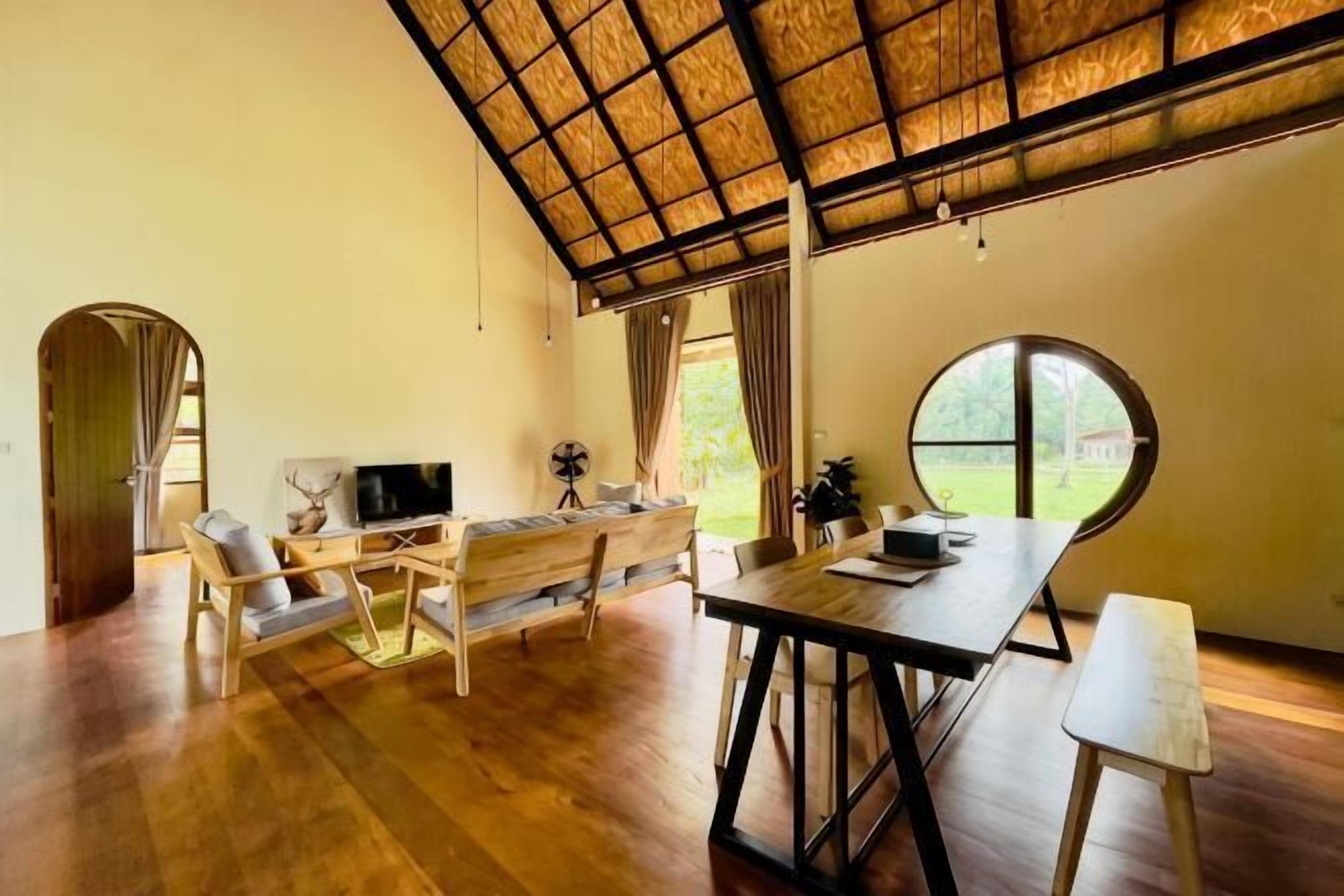 Amplia habitación con techo alto, una mesa de comedor de madera, un televisor y una zona de estar con un gran ventanal.