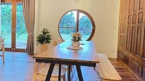 A dining area with a wooden table, chairs, and a large window with a view of greenery. - "Peace in Ranong: Your Cozy Retreat" (Kapoe)