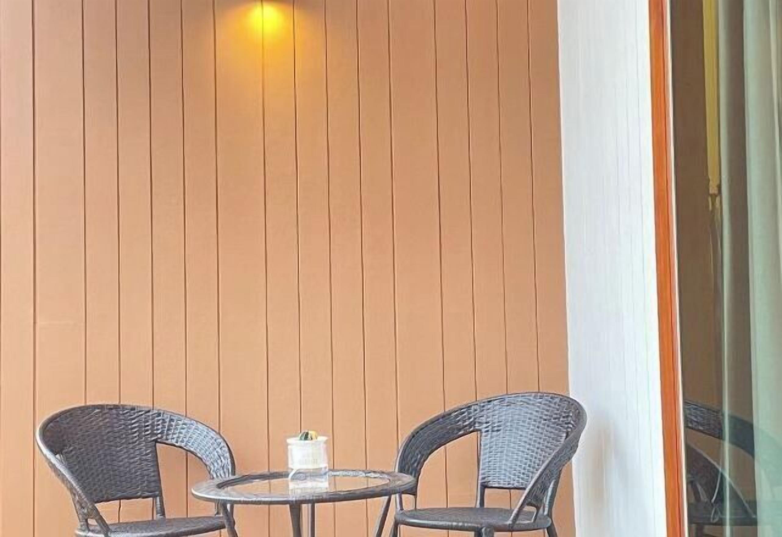 Una pequeña mesa redonda con dos sillas de mimbre, una vela blanca y una pared con listones de madera verticales.