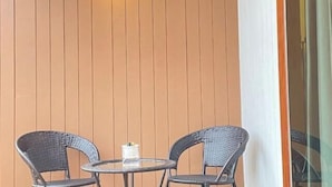 A small round table with two wicker chairs, a white candle, and a wall with vertical wooden slats. - "Peace in Ranong: Your Cozy Retreat" (Kapoe)
