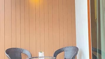 Una pequeña mesa redonda con dos sillas de mimbre, una vela blanca y una pared con listones de madera verticales.