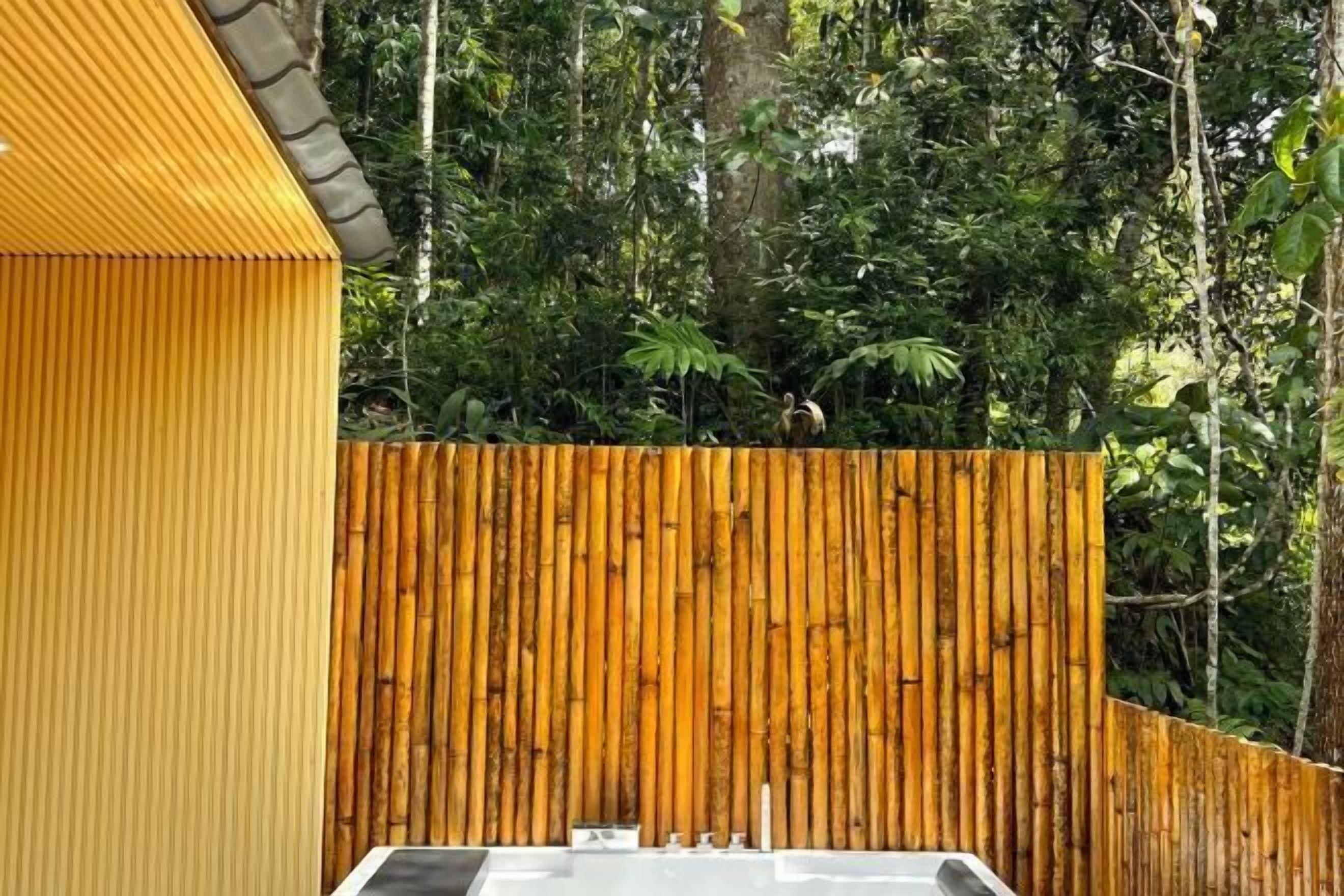 A room with a bamboo wall, a white bathtub, and a yellow exterior wall.