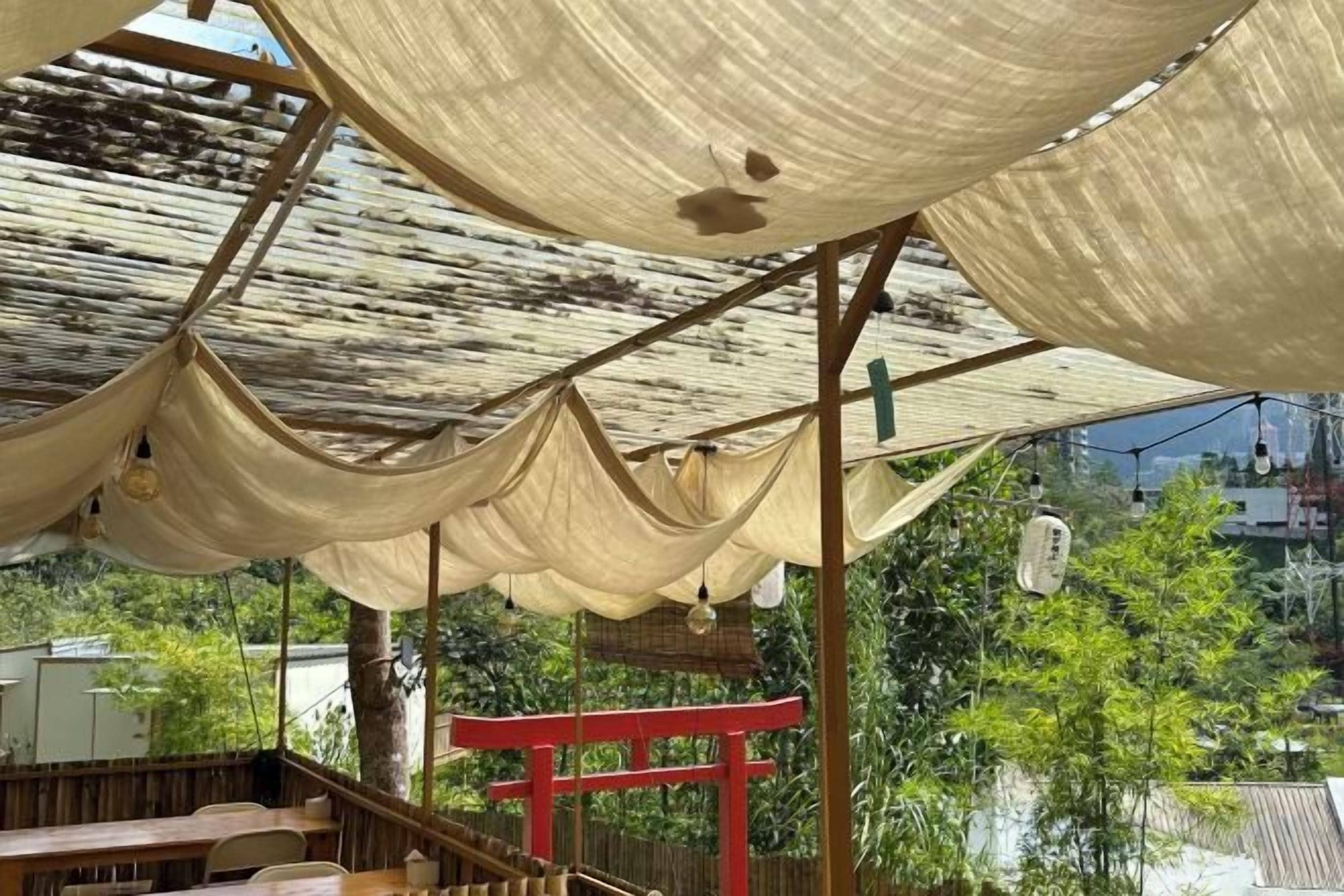 Un espacio al aire libre cubierto con un torii rojo, bancos de madera y vistas a zonas verdes y edificios al fondo.
