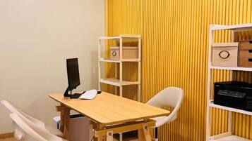 Una habitación con un escritorio de madera, una silla blanca y dos estanterías blancas frente a una pared amarilla a rayas.