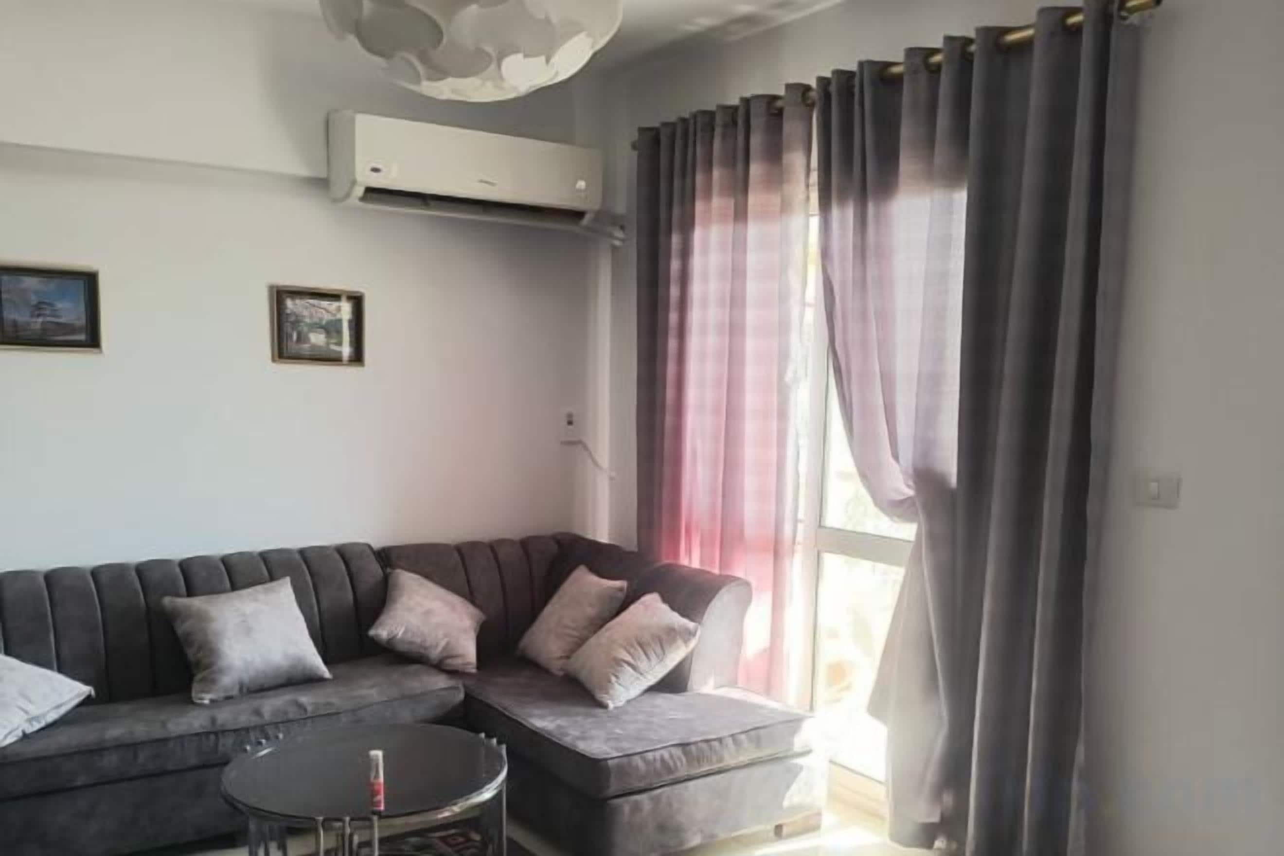A living room with a sectional sofa, a small round table, and a window with curtains.
