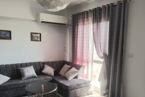 Una sala de estar con un sofá seccional, una mesita redonda y una ventana con cortinas.