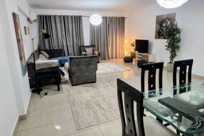 Una sala de estar con un sofá, una mesa de centro y un televisor. Hay un comedor con sillas y una mesa de vidrio.