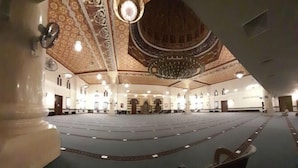 Een ruime, open zaal met een versierd plafond en kroonluchters, vermoedelijk een moskee of een groot openbaar gebouw.