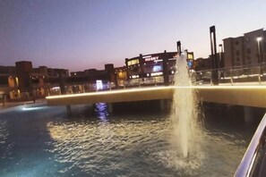 Vista nocturna de una fuente de agua con un puente, iluminada por luces ambientales.