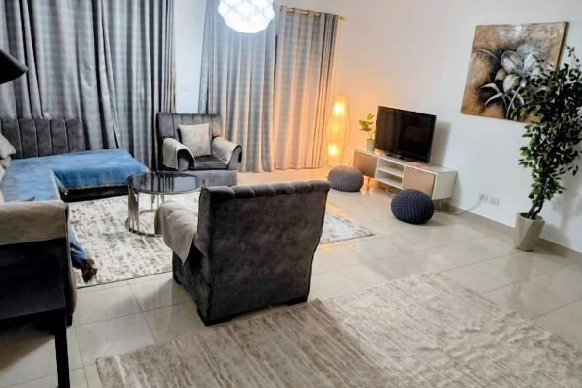 A modern living room with a sofa, armchair, TV, and decorative plants.