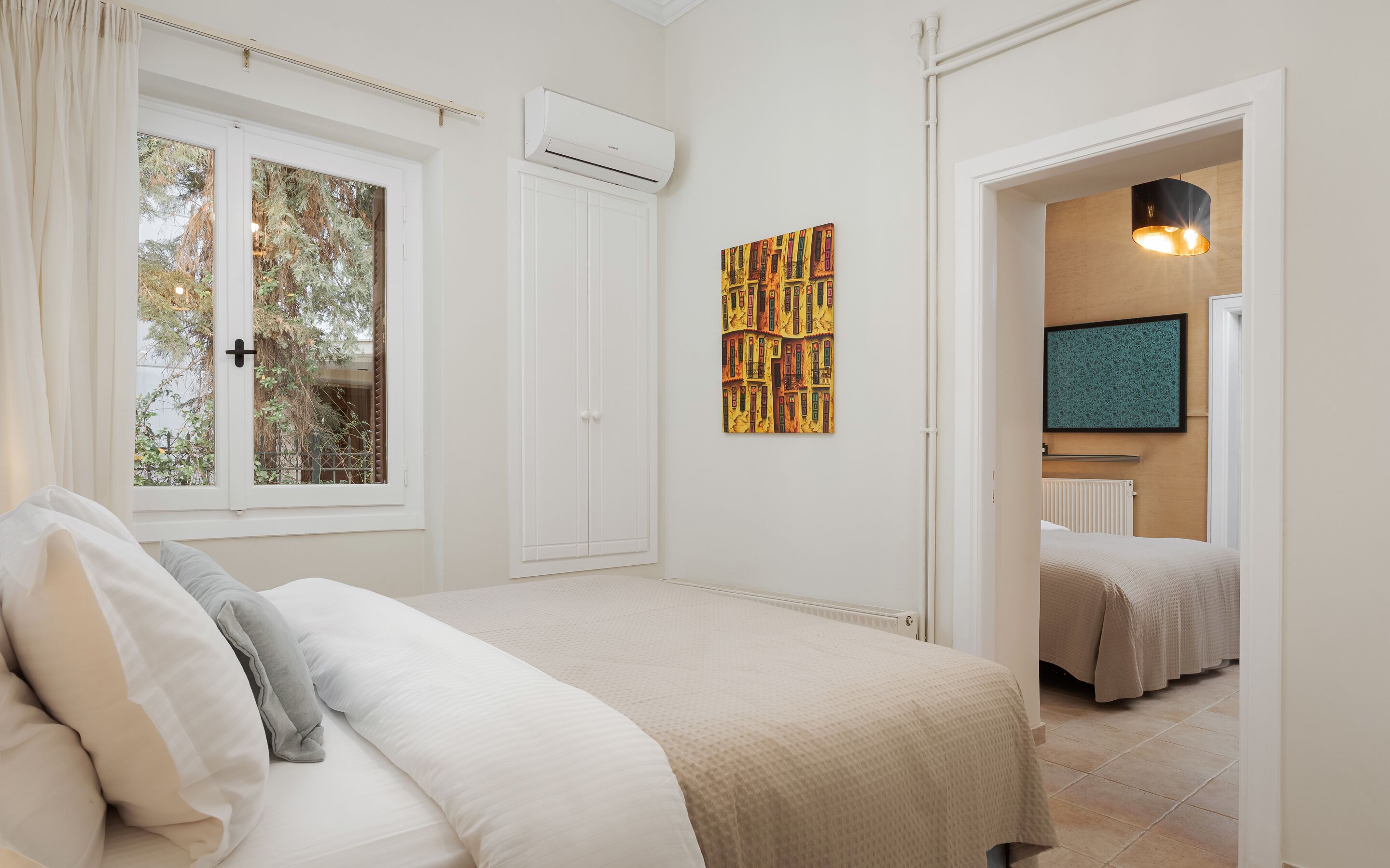 Ein Schlafzimmer mit Bett, Fenster, Klimaanlage, einem Bild und einem Flur, der in einen anderen Raum führt.