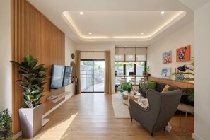 A modern living room with a flat-screen TV, wooden paneling, and a large potted plant.