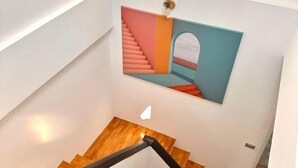 A modern staircase with wooden steps and a black handrail, leading to a wall with a colorful abstract painting. - Stylish Modern Home 4Bedroom 7Bed 200m BTS PhraKhanong, 10min ThongLo (Bangkok)