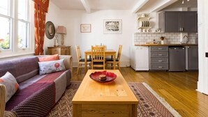 Un salon confortable avec un canapé, une table à manger et des chaises, une cuisine équipée de placards et d’appareils électroménagers, et une grande fenêtre.