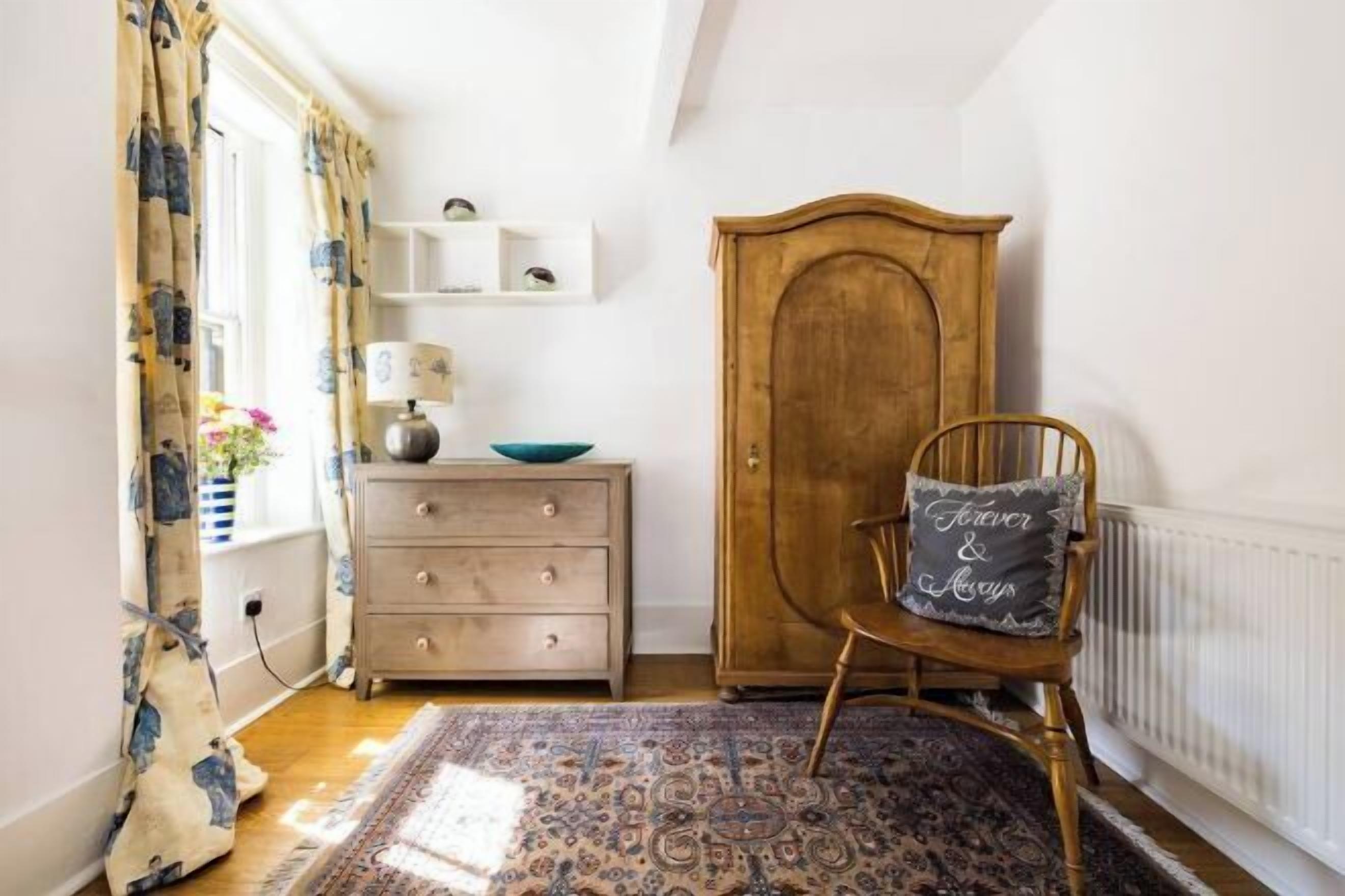 Une pièce chaleureuse avec un meuble en bois, une chaise avec un coussin, une commode et un tapis à motifs.