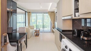 A modern kitchen with a dining area, large windows, and a view of greenery. - 1-bedroom Condo Mida Grand Surin Phuket (Choeng Thale)