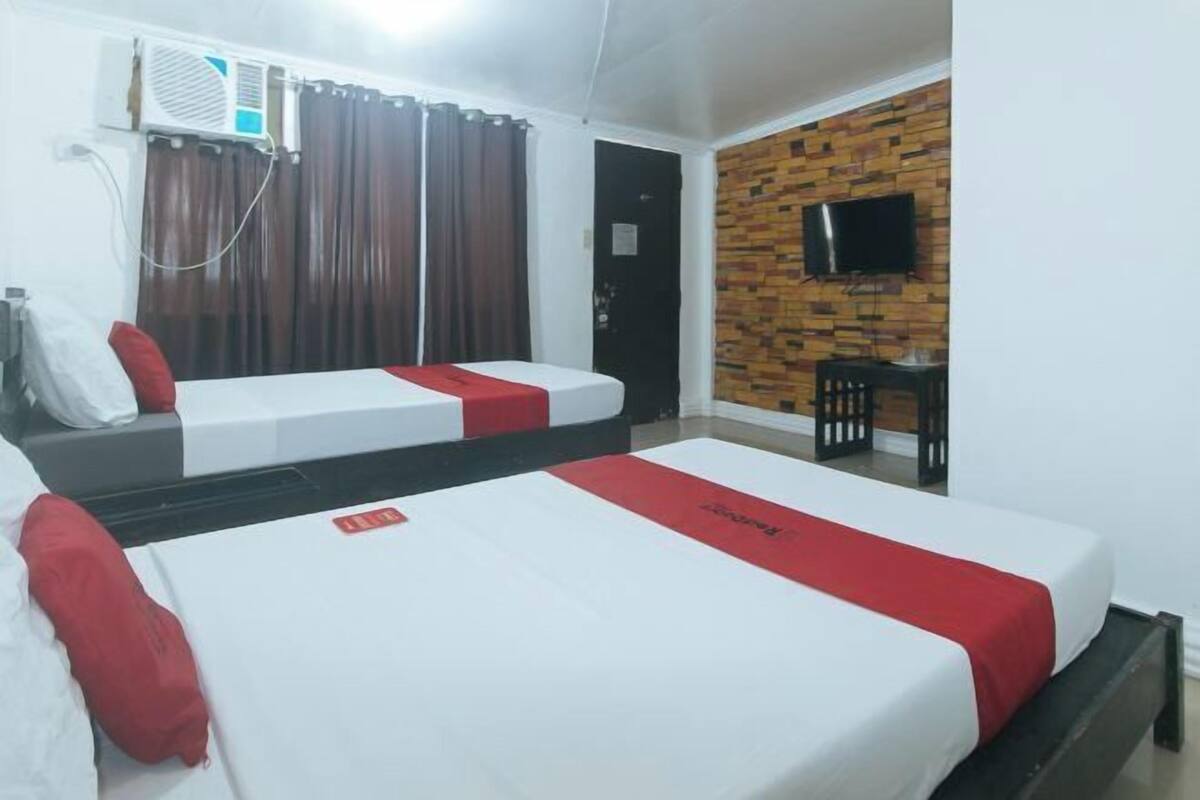 A hotel room with two beds, a TV mounted on the wall, and an air conditioning unit.