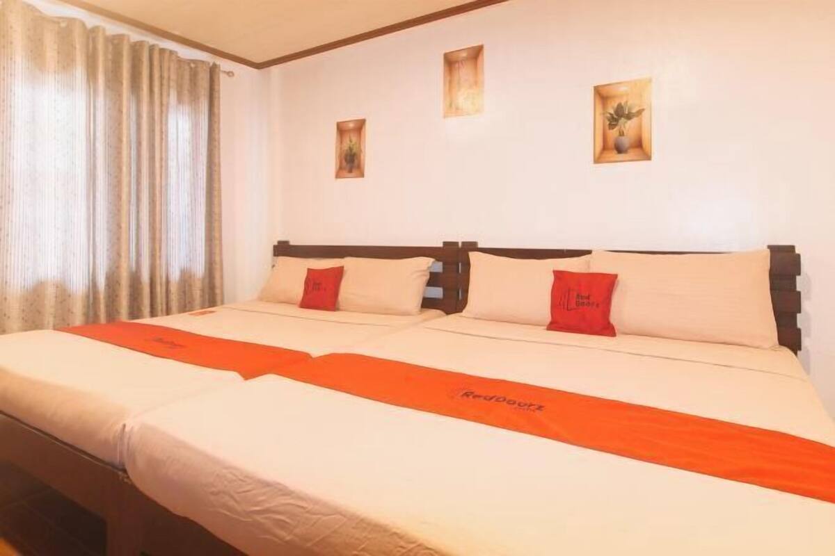 A hotel room with two beds, a red and white bedspread, and a window with curtains.