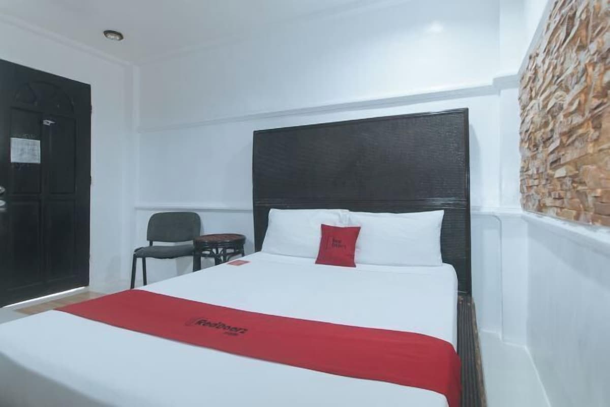A hotel room with a bed, a chair, a small table, and a stone wall.