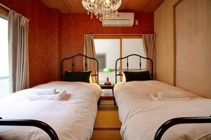 A room with two beds, a chandelier, an air conditioner, and a window with curtains. - Triphome Kinshicho (Tokyo)