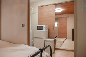 A bedroom with a bed, a microwave, and a wardrobe with a mirror. - Triphome Kinshicho (Tokyo)
