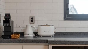 A kitchen with white tiled walls, a toaster, a coffee maker, and a basket on the counter. - Now Aewol (Jeju)