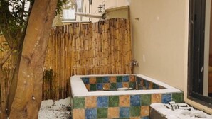 Une petite baignoire extérieure, recouverte de carreaux, entourée de neige et délimitée par une clôture en bambou.