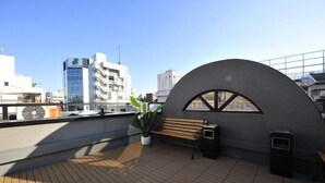 A rooftop terrace with a wooden floor, a bench, a potted plant, and a trash bin. - Asakusa Kei Hotel (Tokyo)