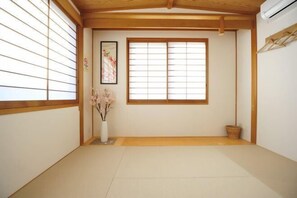 Een traditionele Japanse kamer met tatami vloerbedekking, shoji schermen, een vaas met bloemen en een ingelijste foto aan de muur.