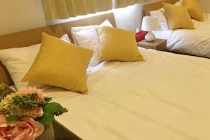 Habitación de hotel con dos camas, una mesita de noche con lámpara y un jarrón con flores.