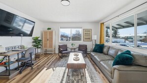 A modern living room with a sofa, coffee table, and chairs, a television, and a window with a view of a snowy landscape. - Remodeled PET Friendly Unit | Near Downtown Palmer (Palmer)
