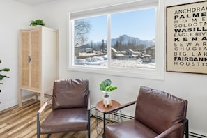 A room with two leather chairs, a wooden cabinet, a small table with a plant, and a window with a view of a snowy landscape.