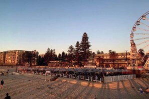 A beach area with a Ferris wheel, umbrellas, and buildings in the background. - Beach & Bay - Modern Family Stay Glenelg North (Glenelg North)