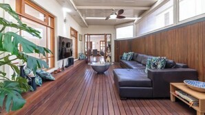 A spacious living area with a wooden floor, a sofa, a coffee table, and a television. - Beach & Bay - Modern Family Stay Glenelg North (Glenelg North)