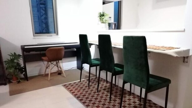 A dining area with a piano, four chairs, a patterned rug, and a small table with a plant.