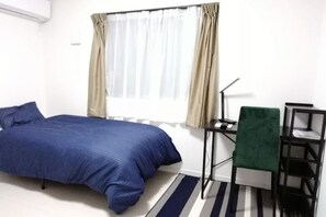 A single bed with a blue bedspread, a desk with a chair, a lamp, and a window with curtains. - WZRE House (Entire only) (Kawasaki)